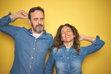 Obraz premium Beautiful middle age couple together standing over isolated yellow background stretching back, tired and relaxed, sleepy and yawning for early morning