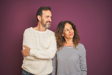 Beautiful middle age couple wearing winter sweater over isolated purple background smiling looking to the side and staring away thinking.