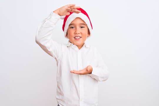 Beautiful Kid Boy Wearing Christmas Santa Hat Standing Over Isolated White Background Gesturing With Hands Showing Big And Large Size Sign, Measure Symbol. Smiling Looking At The Camera