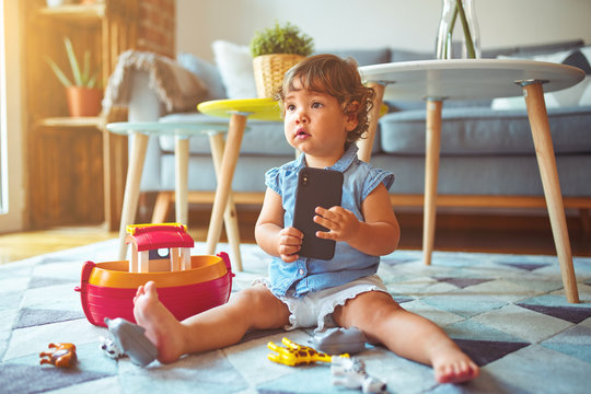 Beautiful toddler child girl sitting on the carpet playing with smartphone
