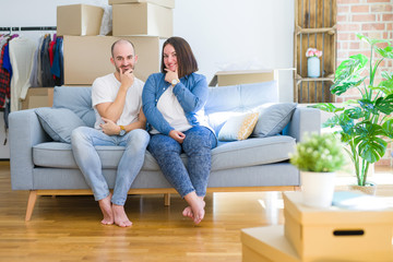 Fototapeta na wymiar Young couple sitting on the sofa arround cardboard boxes moving to a new house looking confident at the camera with smile with crossed arms and hand raised on chin. Thinking positive.