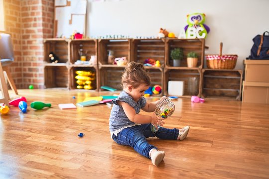 Beautiful toddler sitting on the floor with jar of chocolate colored balls at kindergarten
