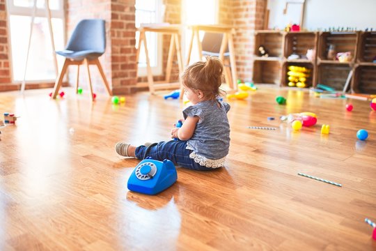 Beautiful toddler sitting on the floor playing with vintage phone at kindergarten