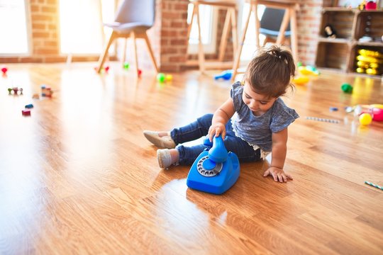 Beautiful toddler sitting on the floor playing with vintage phone at kindergarten