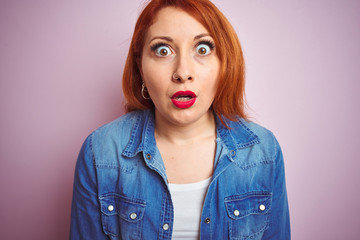 Youg beautiful redhead woman wearing denim shirt standing over isolated pink background afraid and shocked with surprise expression, fear and excited face.