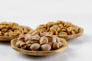 wood plates of salted peanuts and pistachios on white background. snack to beer