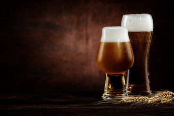 two glasses of cold dark beer and wheat spikelets on dark background. copy space