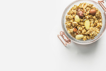Homemade Granola Muesli with oats dried fruits coconut flakes hazelnuts almonds walnuts mixture in glass jar on white table. Healthy wholesome food fiber energy source