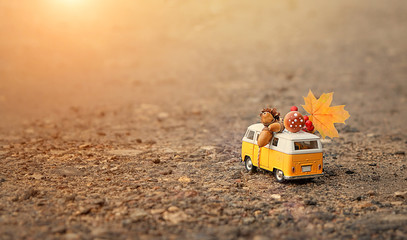 classic yellow bus on road. toy retro bus with maple leaf, cone, mushroom, acorn. autumn season concept. fall time. vacation adventure and travel concept. soft focus