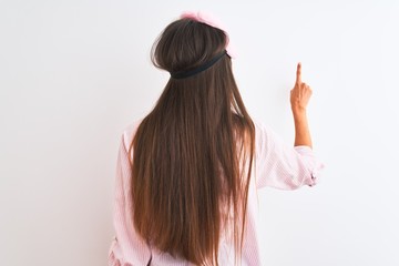 Young beautiful woman wearing sleep mask and pajama over isolated white background Posing backwards pointing ahead with finger hand