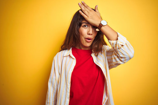 Young beautiful woman wearing red t-shirt and stripes shirt over yellow isolated background surprised with hand on head for mistake, remember error. Forgot, bad memory concept.