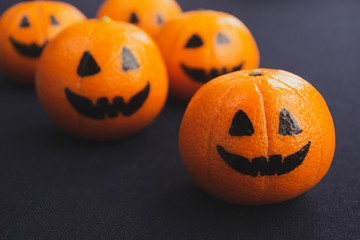 Halloween holiday concept. Painted funny faces on tangerines for Halloween on a dark background