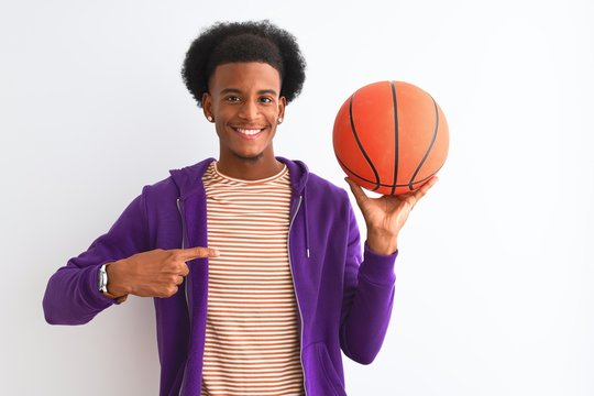 Young african american sportsman holding basketball ball over isolated white background with surprise face pointing finger to himself