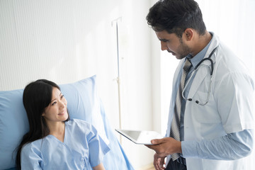 Doctor is talking with young female patient and taking notes while in his office.