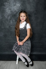 Portrait of a cute little kid girl on a gray background. Child schoolgirl looking at the camera. The concept of education. Copy space.