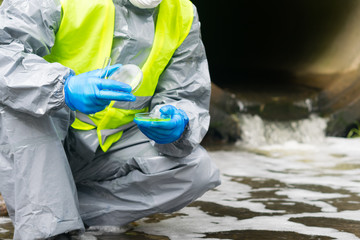 against the background of the suit, the hands of the scientist in protective blue gloves, close the Petri dish with biomaterials