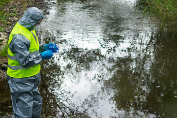 scientist in a protective suit and mask, holding a set of test tubes with water samples treatment...