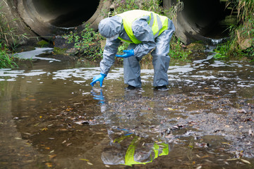 scientist in a protective suit and mask, collects the liquid from the reservoir in a test tube, to take tests in the laboratory