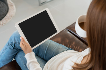 Obraz premium Young woman is relaxing on comfortable couch and using tablet at home.