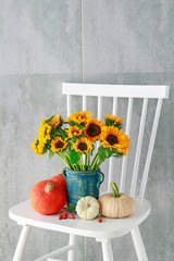 Bouquet of sunflowers and colorful pumpkins on white wooden chair.