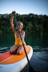 SUP Stand up paddle board concept - Pretty, young woman paddle boarding on a lovely lake in warm...