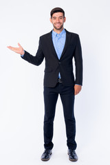 Full body shot of happy young bearded Persian businessman showing something