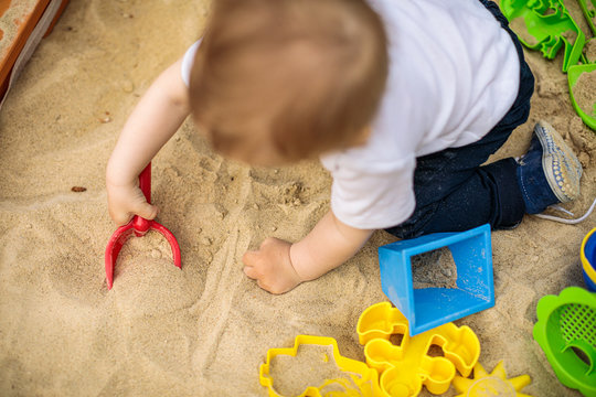Little kid playing in sand with many plastic toys