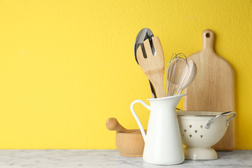Different kitchen utensils on marble table against yellow background. Space for text