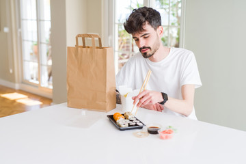 Young man eating sushi asian food and noodles using choopsticks from take away delivery