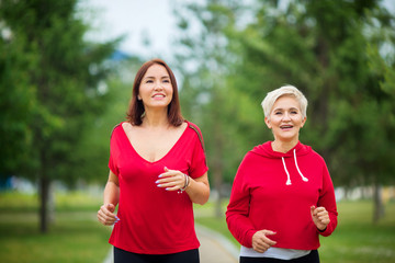 two adult women in sportswear run in the summer park