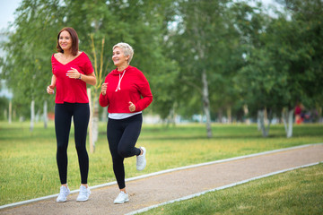 two adult women in sportswear run in the summer park
