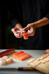 Nahaufnahme der Chefhände, die japanisches Essen vorbereiten. Japanischer Koch macht Sushi im Restaurant. Junger Koch, der traditionelles japanisches Sushi auf Schneidebrett macht
