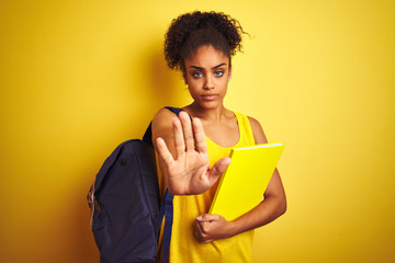 American student woman wearing backpack holding notebook over isolated yellow background with open...