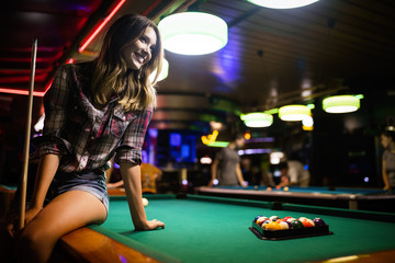 Young beautiful girl is playing billiards. Pleasant pastime, rest, entertainment.