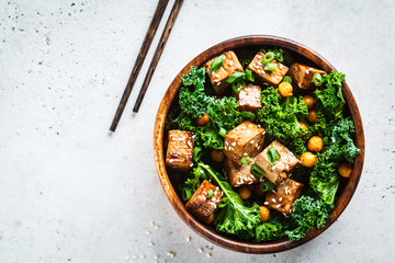 Teriyaki tofu salad with kale and chickpeas in a wooden bowl, copy space, top view.
