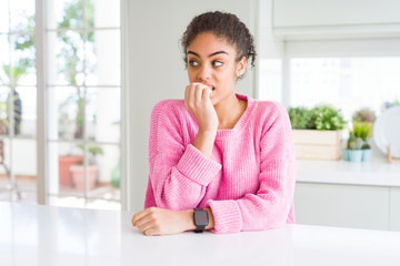 Beautiful african american woman with afro hair wearing casual pink sweater looking stressed and nervous with hands on mouth biting nails. Anxiety problem.