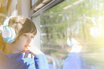 the girl looks out the window of the train and listening to music in headphones.
