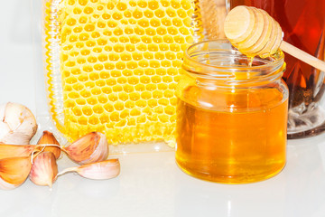 Honey and pieces of garlic on the background of honeycomb. Honey in a glass jar and honeycomb.
