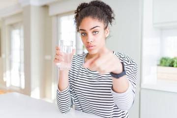 Young african american girl drinking a fresh glass of water pointing with finger to the camera and to you, hand sign, positive and confident gesture from the front