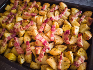 Appetizing baked potato with bacon on a baking sheet close-up. The concept of delicious high-calorie food.