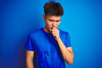 Young asian chinese man wearing t-shirt standing over isolated blue background feeling unwell and coughing as symptom for cold or bronchitis. Healthcare concept.