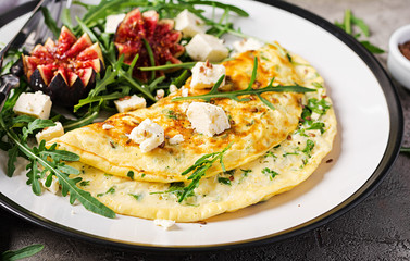 Omelette with feta cheese, parsley and salad with figs, arugula on white plate. Frittata - italian omelet.