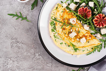 Omelette with feta cheese, parsley and salad with figs, arugula on white plate. Frittata - italian omelet. Top view. Flat lay.