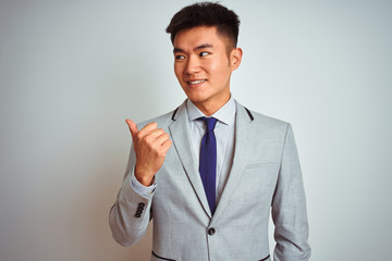 Asian chinese businessman wearing suit and tie standing over isolated  background smiling with happy face looking and pointing to the side with thumb up.