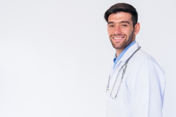 Profile view of happy young bearded Persian man doctor looking at camera