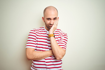 Young bald man with beard wearing casual striped red t-shirt over white isolated background thinking looking tired and bored with depression problems with crossed arms.