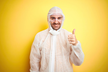 Naklejka premium Young man wearing painter equipment and safety glasses over isolated yellow background happy with big smile doing ok sign, thumb up with fingers, excellent sign