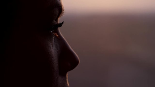 Woman thinking and looking out from train window, extreme close up shot of her eye. Blurred background, dim natural light at evening time. High speed carriage run fast, slow motion shot