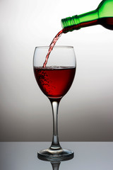 Pouring red wine into the wineglass close-up, isolated on light gradient background