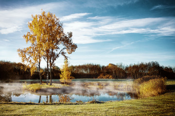 Autumn landscape with trees and lake with fog. Frost covered ground.